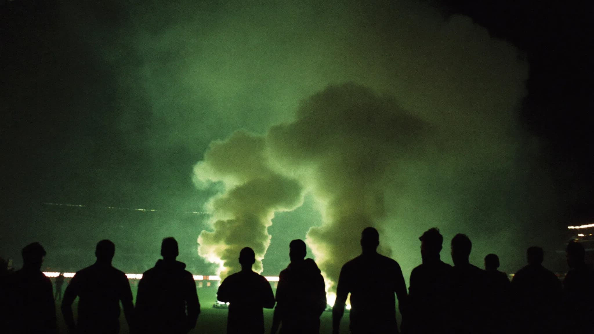 Tribune de supporters dans la fumée verte, sous les projecteurs